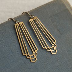 These great earrings are made with solid brass and feature a graduated art deco design.  They remind us of classic Deco architecture, like the Chrysler building!   The earrings measure 45mm (just under two inches) in length and have gold plated ear wires.   They have been designed and made in our Edinburgh studio.   This piece of handmade jewellery comes packaged in a nice recycled gift box with a handmade tag, all ready to give or keep. We also have these earrings in silver, as well as  many other Art Deco designs!  🖤 FASTER SHIPPING 🖤 Need this fast? We offer a Faster Shipping option here: https://www.etsy.com/uk/listing/100107311/faster-shipping-priority-post-upgrade 🖤 GIFT MESSAGE & WRAP SERVICE! 🖤 https://www.etsy.com/uk/listing/750160511/gift-wrap-wrapping-personalised-card?ref=l Art Deco Style Jewelry, Gold Wire Earrings, Retro Brass Earrings, Gold Brass Art Deco Earrings, Retro Brass Drop Earrings, Retro Brass Jewelry With Matching Earrings, Art Deco Gold Brass Jewelry, Handmade Brass Art Deco Earrings, Art Deco Brass Jewelry With Matching Earrings