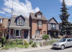 two cars are parked on the street in front of three houses with white picket fence