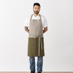 a man wearing an apron standing in front of a white wall with his hands on his hips