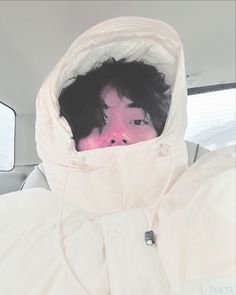 a man with black hair wearing a white jacket and pink hood in the back of a car