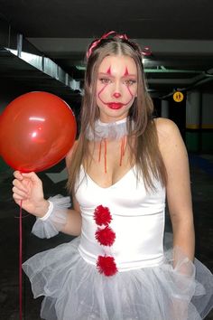 a woman dressed up as a clown holding a red balloon and wearing a white dress