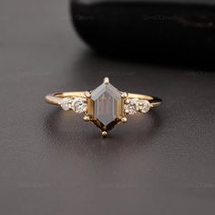 a gold ring with an emerald stone surrounded by white diamonds on a black surface next to a rock