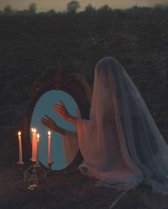 a woman with her hands on the mirror and candles in front of her, while she is wearing a veil