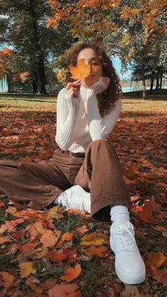 a woman sitting on the ground with leaves in front of her and holding a leaf up to her face