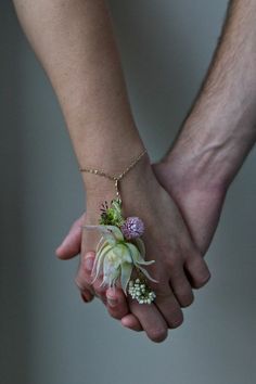 two people holding hands with small flowers on their wrist and one is holding the other's hand