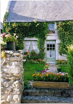 an old stone house with flowers and plants growing on the front door, along side it