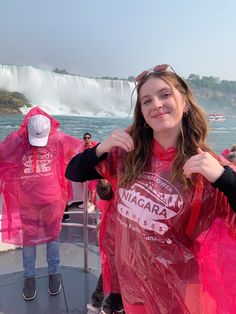 a woman in pink raincoats standing on the side of a boat with niagara falls behind her