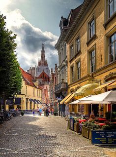 a cobblestone street lined with buildings and people walking around it on a cloudy day