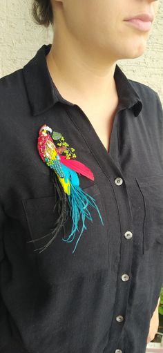 a woman wearing a black shirt with a colorful bird on it's lapel