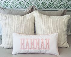 two pillows with the word hannah on them sit on a bed in front of a wallpapered headboard