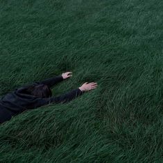 a person laying in the grass with their arms out and hands outstretched to reach for something