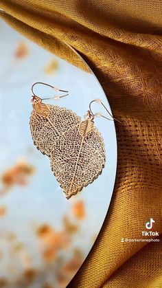 a pair of earrings hanging from the side of a piece of cloth with leaves on it