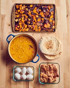 an assortment of food including eggs, bread and soup in pans on a wooden table