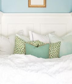 a white bed topped with lots of pillows next to a framed picture on the wall