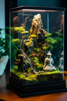 a small glass case with moss and rocks in the center on a wooden table next to a potted plant