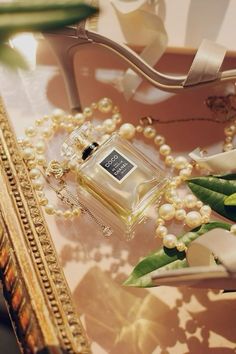 a bottle of perfume sitting on top of a glass table next to flowers and pearls