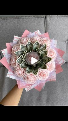 someone is holding a bouquet made out of money and pink roses with green leaves on it