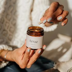 a woman is holding a jar with some white nail polish on it and her hands are in the air