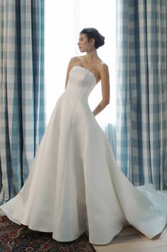 a woman standing in front of a window wearing a wedding dress