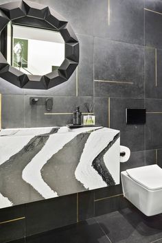 a modern bathroom with black and white tiles on the wall, toilet and mirror above it