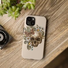 a phone case that has a skull and flowers on it next to a camera, with a plant in the background