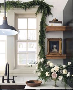 flowers and greenery are arranged in front of an open window on the kitchen counter