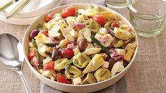 a white bowl filled with pasta salad next to silverware and utensils on a table