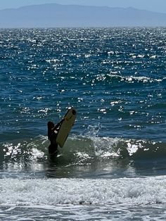 a person riding a surfboard on top of a wave in the ocean with mountains in the background