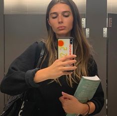 a woman is taking a selfie in the mirror with her cell phone while holding a book