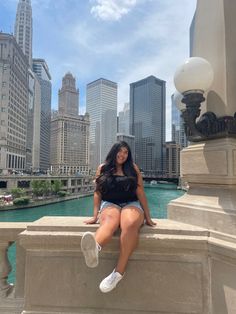 a woman sitting on top of a stone wall next to a river and tall buildings