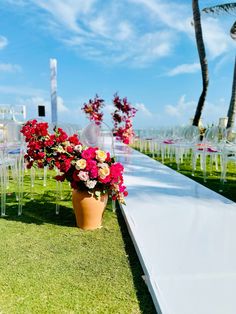 an aisle lined with chairs and flowers on the grass, in front of palm trees