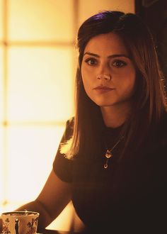 a woman sitting at a table with a glass in front of her and looking off to the side