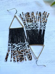 two pairs of beaded earrings on top of a white wooden table next to a plant