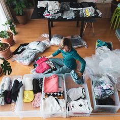 a woman sitting on the floor in front of some clothes and other items that she is packing