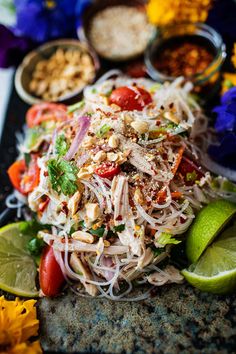 a salad with shredded noodles, tomatoes, onions and limes on a black platter