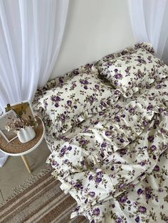 an unmade bed with purple flowers on it