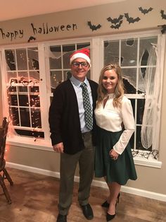 a man and woman standing next to each other in front of a window decorated for halloween