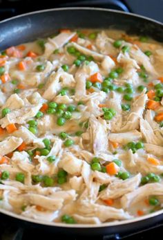 a skillet filled with chicken, peas and carrots