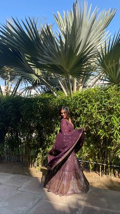 a woman standing in front of a palm tree wearing a purple sari and matching heels