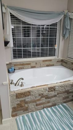 a bath tub sitting under a window next to a rug