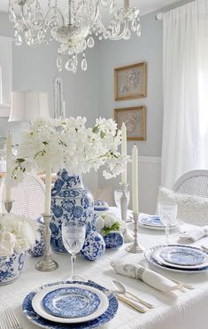 a dining room table set with blue and white plates, silverware, candlesticks and flowers