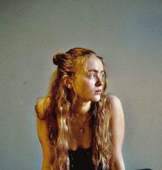 a woman with long red hair sitting on a bed looking off into the distance while wearing a black tank top