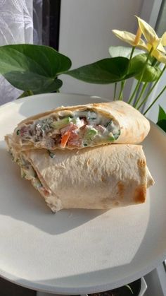 a burrito sitting on top of a white plate next to a yellow flower and potted plant