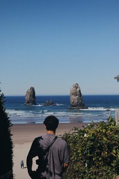 a man standing on top of a sandy beach next to the ocean with two large rocks in the background