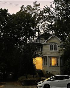 a white car is parked in front of a house with yellow light coming from the windows