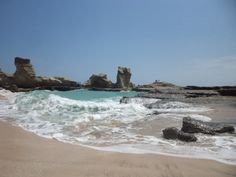 the water is splashing on the beach and rocks