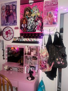 a pink desk and chair in a room with barbie dolls on the wall behind it