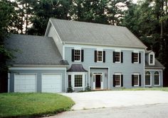 a two story house with white trim and black shutters on the front, surrounded by trees