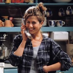 a woman talking on a cell phone while standing in front of a shelf filled with dishes