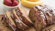 sliced loaf of strawberry banana bread sitting on top of a cutting board next to bananas and strawberries